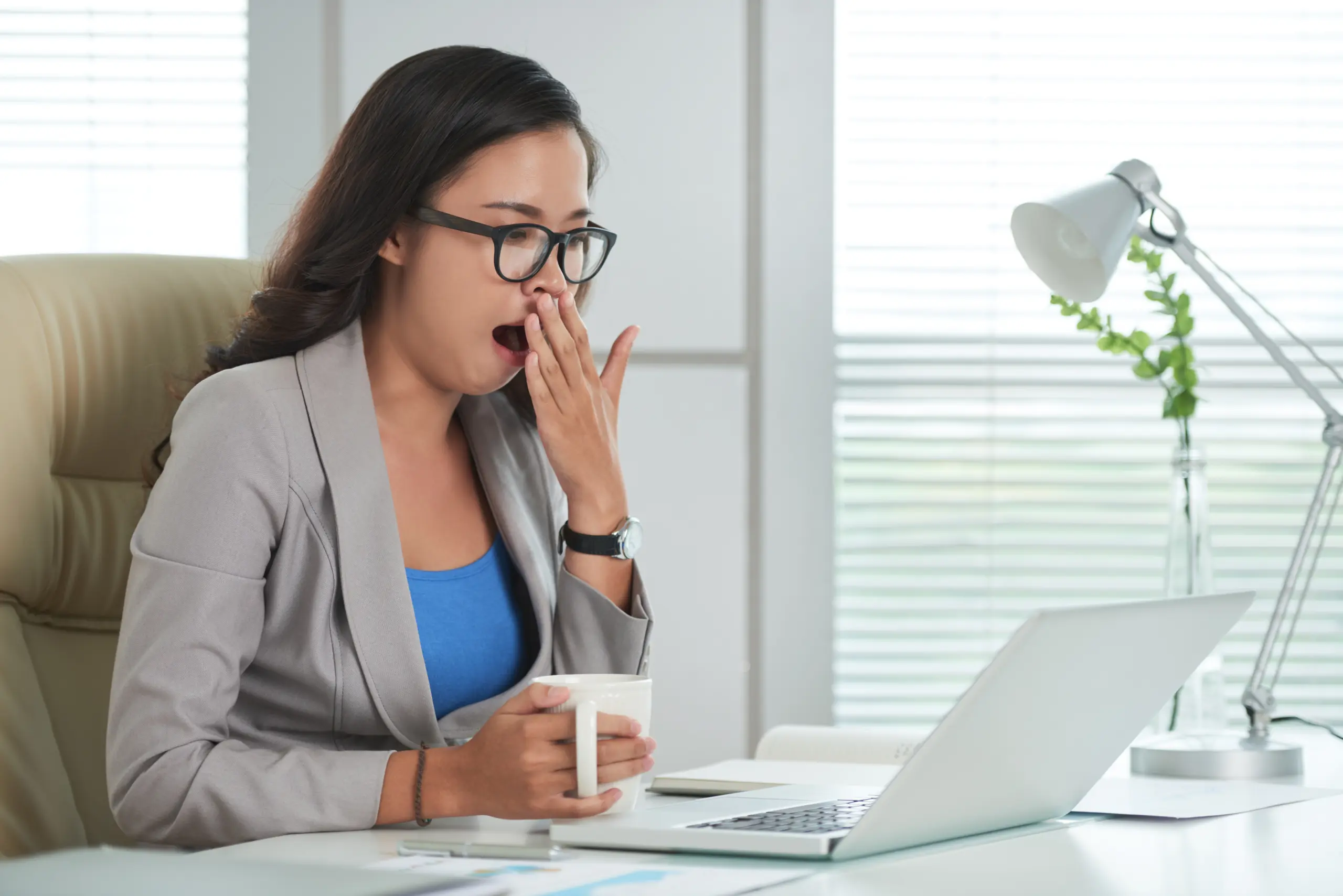 asian-woman-sitting-desk-office-looking-laptop-screen-yawning